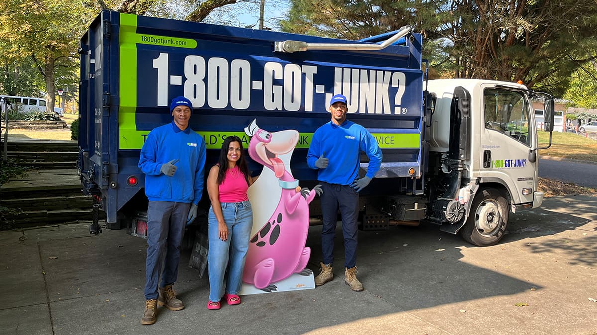 Dina Younis with two 1-800-GOT-JUNK? Truck Team Members and a life size Dino cut-out
