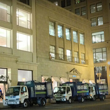 Three 1-800-GOT-JUNK? trucks at a commercial junk removal job at night in the city