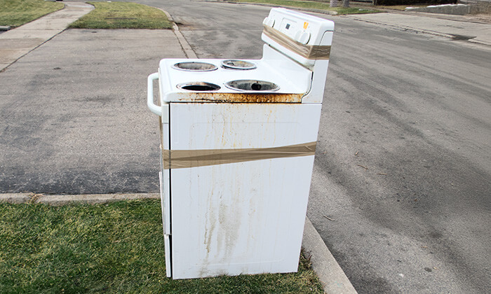 1-800-GOT-JUNK? hauls away an old stove with an appliance dolly.