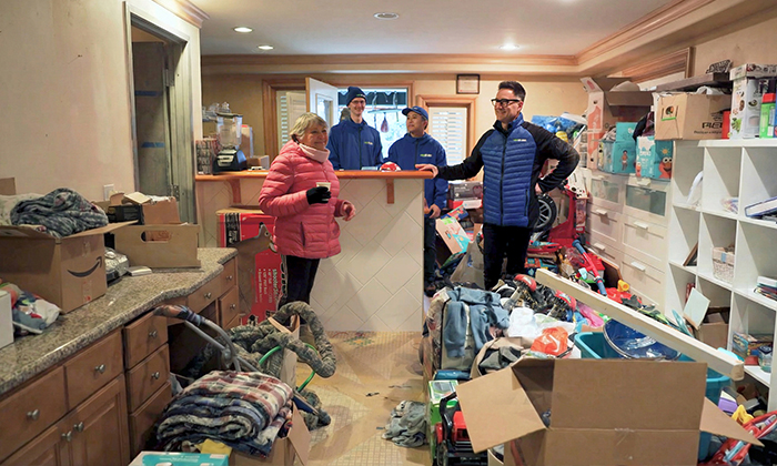  A woman standing in her cluttered home with 1-800-GOT-JUNK? Founder, Brian Scudamore, and two Truck Team Members as she looks at the junk she wants removed.