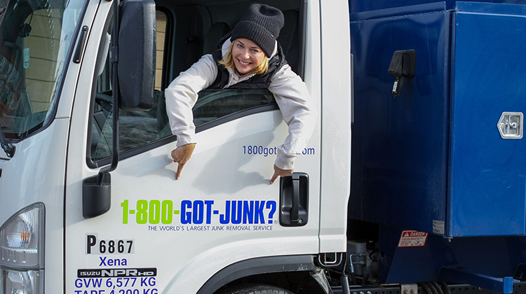 Sarah leaning out of the 1-800-GOT-JUNK? truck to point at the logo on the truck door