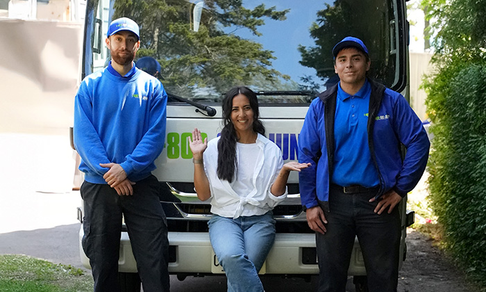A woman and two 1-800-GOT-JUNK? Truck Team Members smiling in front of the truck